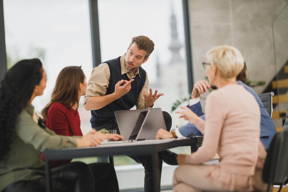 A team leader speaking to colleagues around a table with laptops